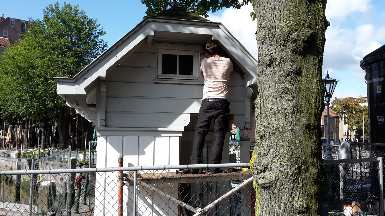 Timmerman haalt rotte stukken hout weg van de gevel van een brugwachtershuisje